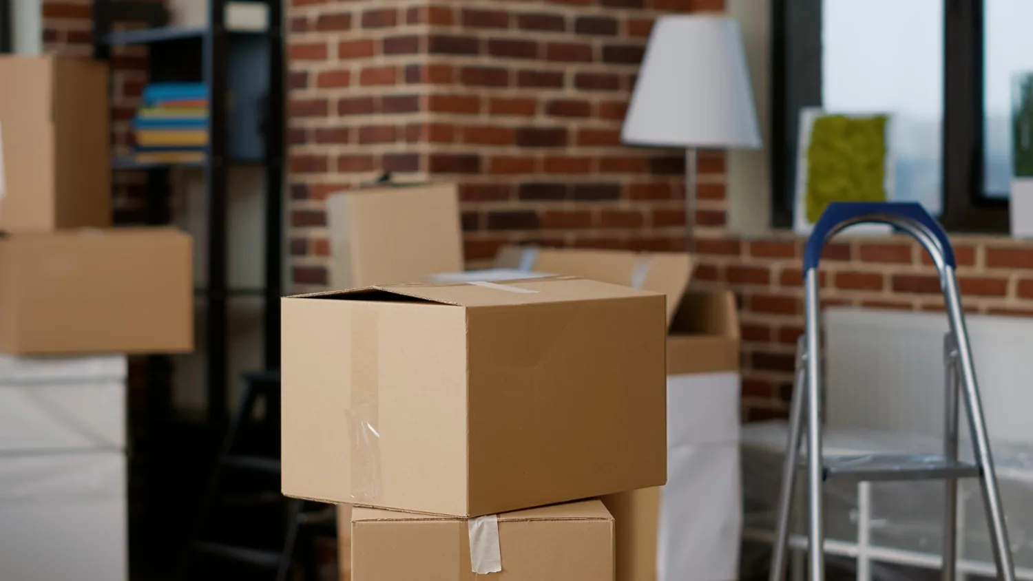Cajas de mudanza apiladas en un salón con pared de ladrillo, listas para el traslado